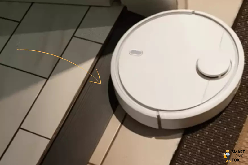 A robot vacuum cleaner crosses a doorstep with the aid of a doorstep ramp.